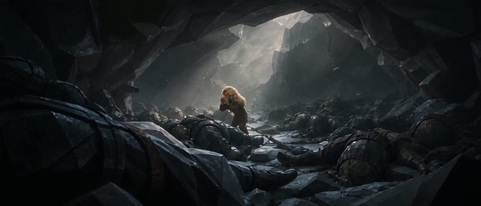 A girl among bodies at a cave mouth.